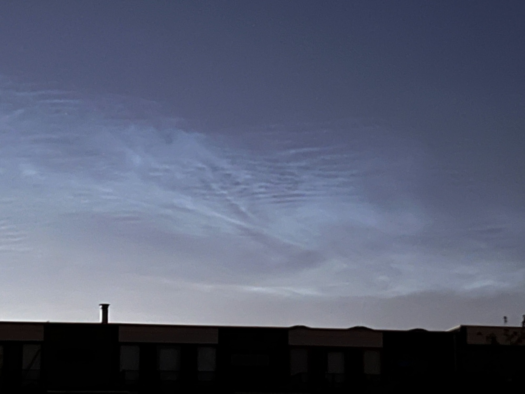 Bluish white noctilucent clouds showing bright mackarel patterns against a dark twilight midnight sky.