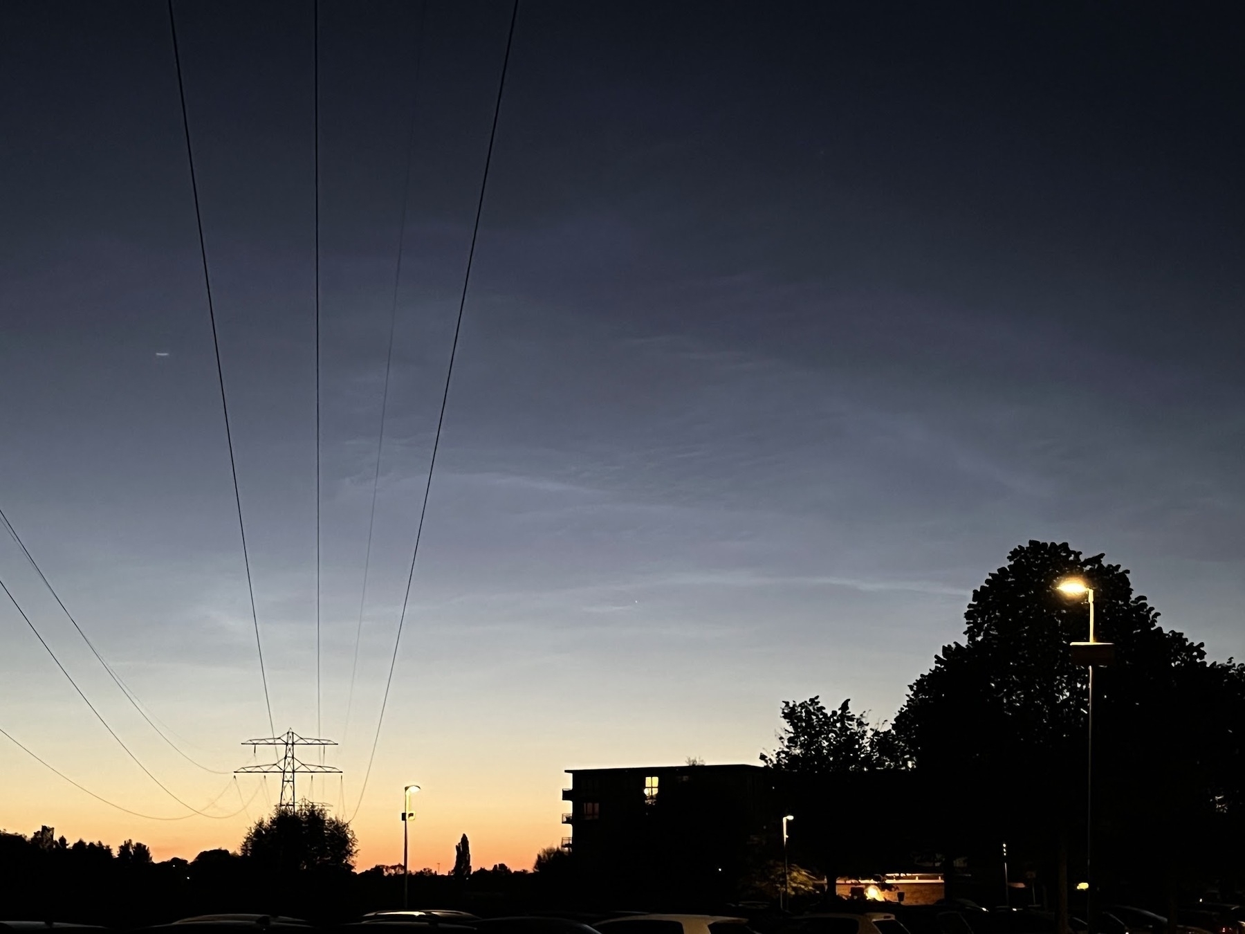 Thin white clouds over electrical pyolons against a midnight sky, deep twilight from black to deep orange at the bottom.