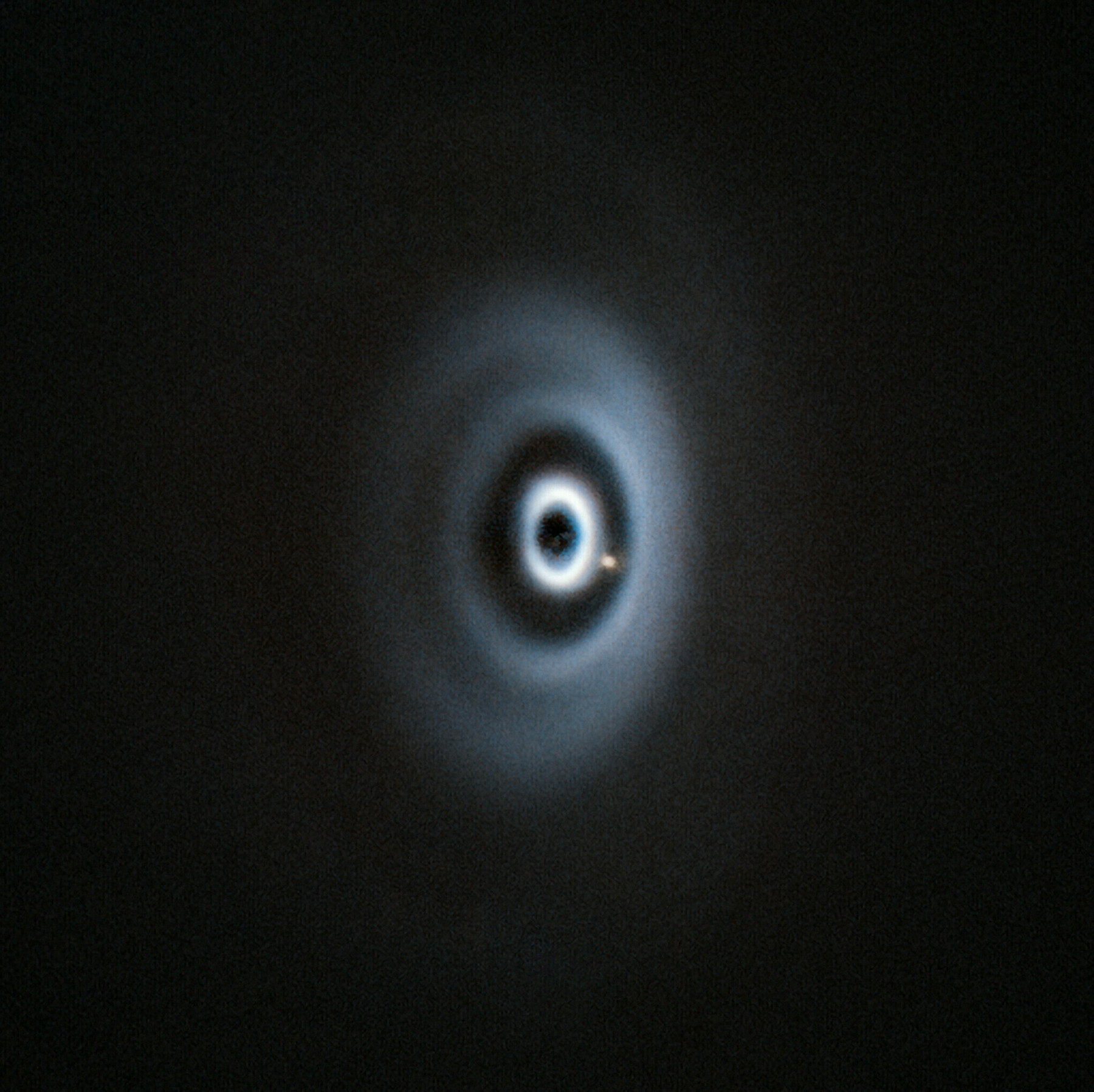 A series of concentric black and white ovals against a black background, with a dim red dot in the lower left of one of the paths of a black ring. The ovals are dust rings around a young star, and the red dot is a 5 Jupiter mass exoplanet called WISPIT 2b.