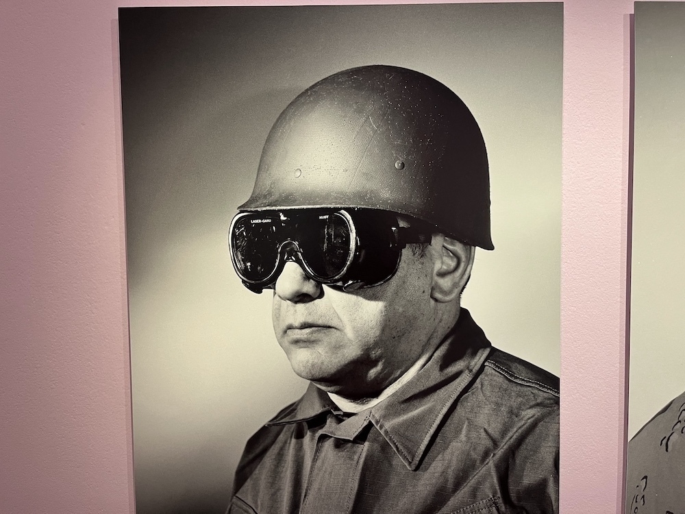 A middle aged man wearing a metal helmet and what looks like welders glass in ski giggles. It is a photo from the 1950's showing army equipment.