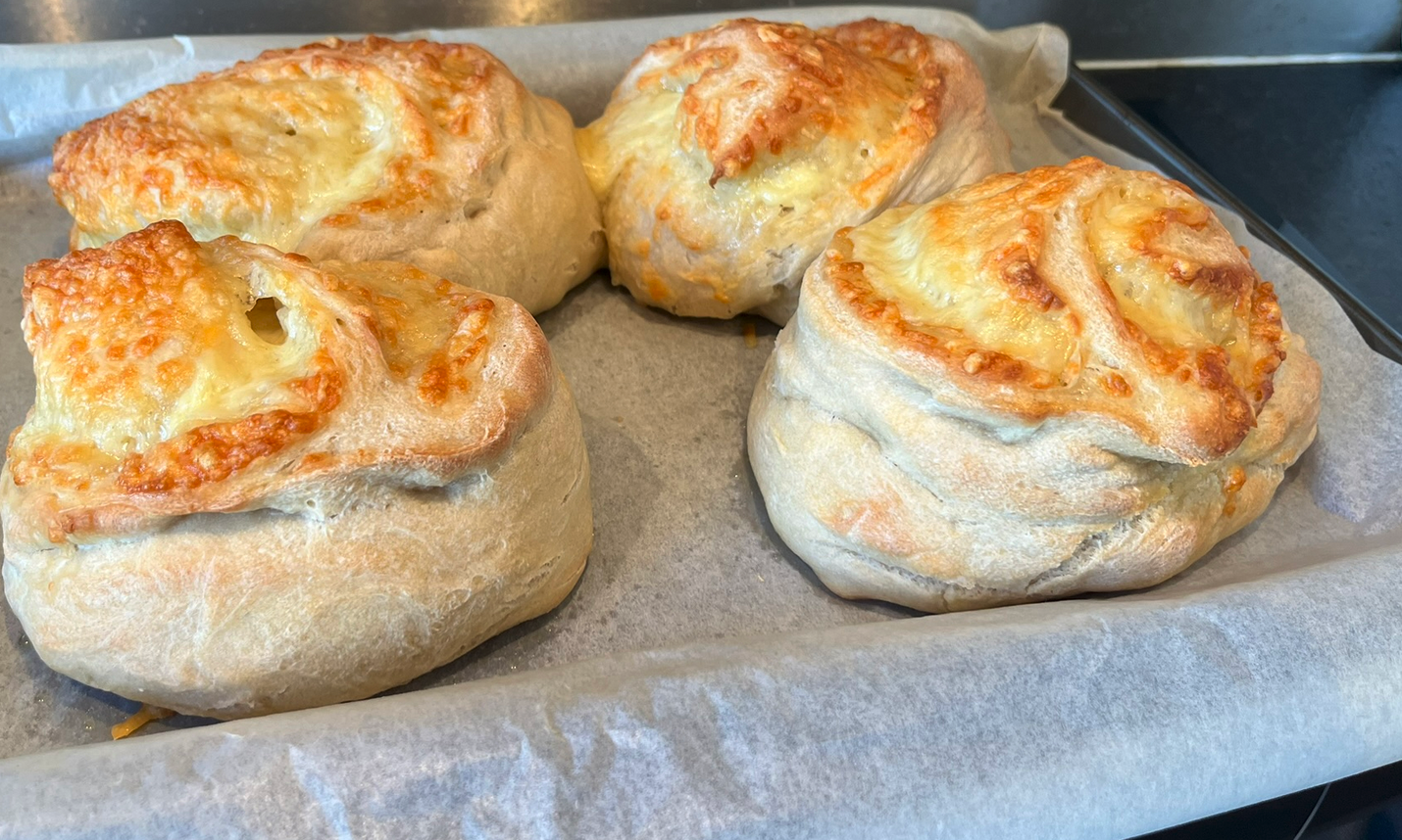 Four small loaves of white bread with partially toasted gruyère cheese oozing out of the top of them.
